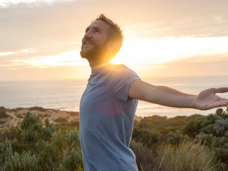 happy man standing by ocean enjoying sunset with arms outstretched