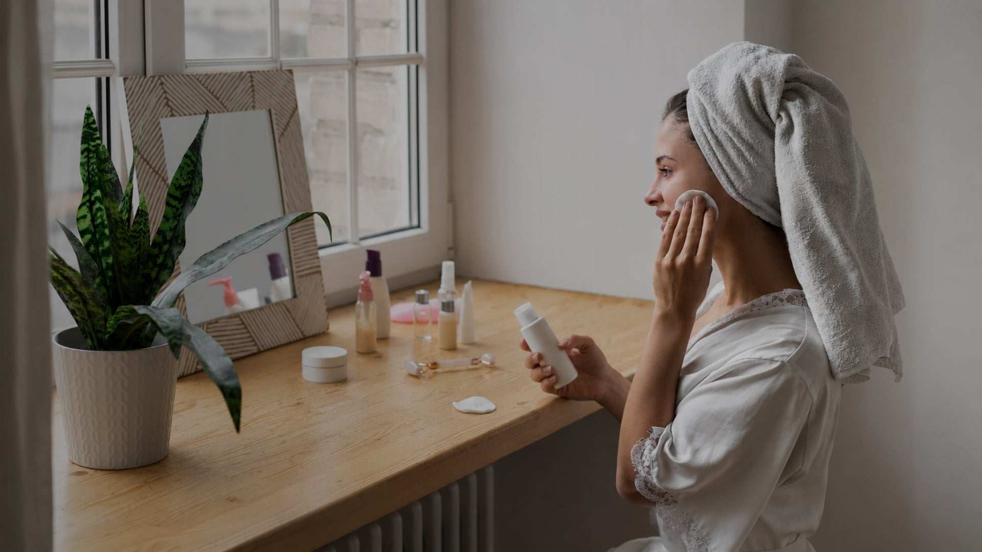 woman with towel on head using cotton pad for skincare
