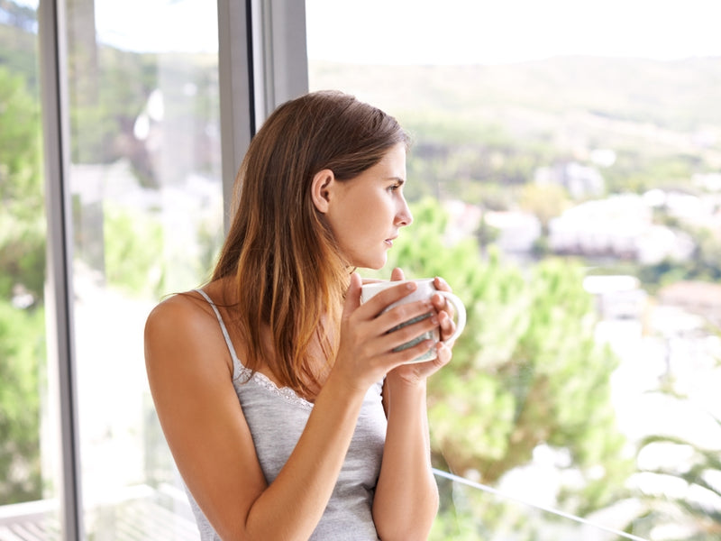 young woman holding a white coffee mug while looking outside